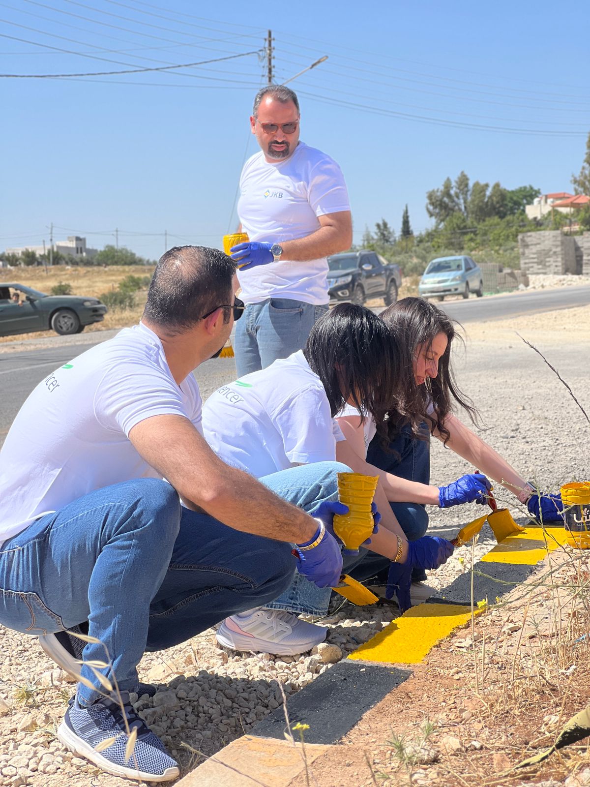 البنك الاردني الكويتي ينفذ حملة لموظفيه لطلاء أرصفة مساره المتبنى على طريق السلط-ارميمين